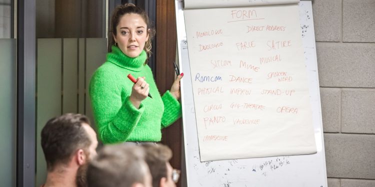 The course tutor is stood at the front of the class writing on a flipchart