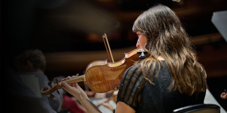 The back of a strings student on stage playing the violin
