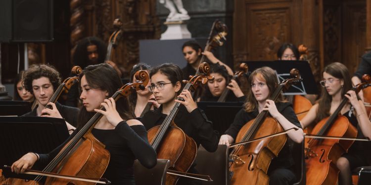 Young male and female cellists playing in an orchestra, sat down, wearing black