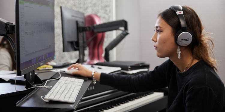 Person using a computer while wearing headphones, seated at a digital piano.