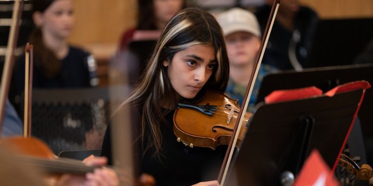 Young female violinist with blonde streak in hair playing in an ensemble