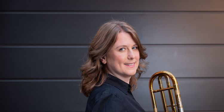Helen Vollam wearing a black shirt and holding their trombone 