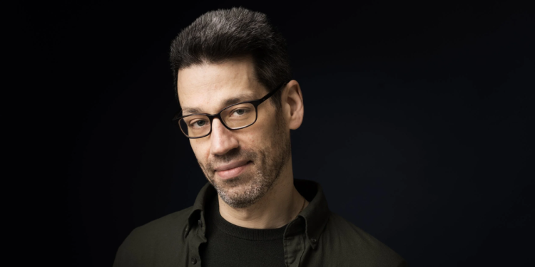 headshot of Jonathan Biss smiling at the camera with a black background