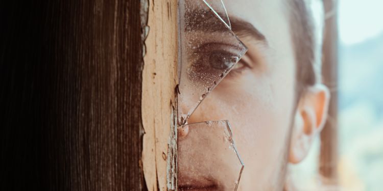 A young man looks through a broken window