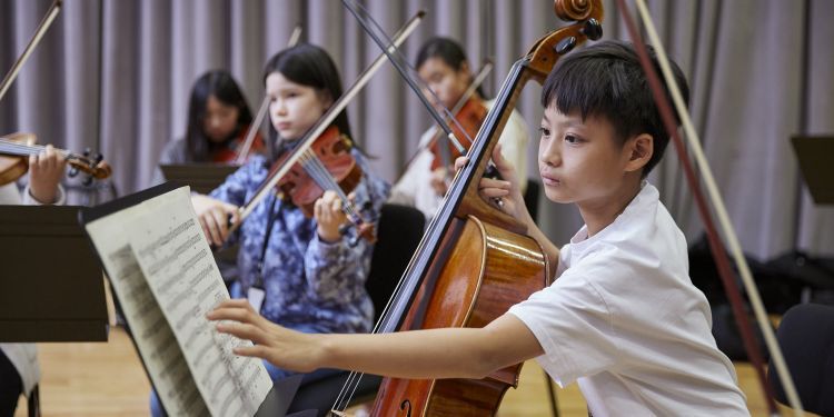 A boy plays the cello and turns a page of his music