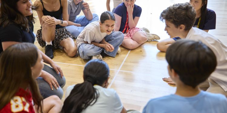 Lots of young people sat on the floor in a large bright room