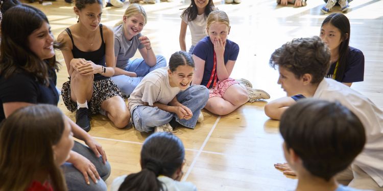 Lots of young people sat on the floor in a large bright room