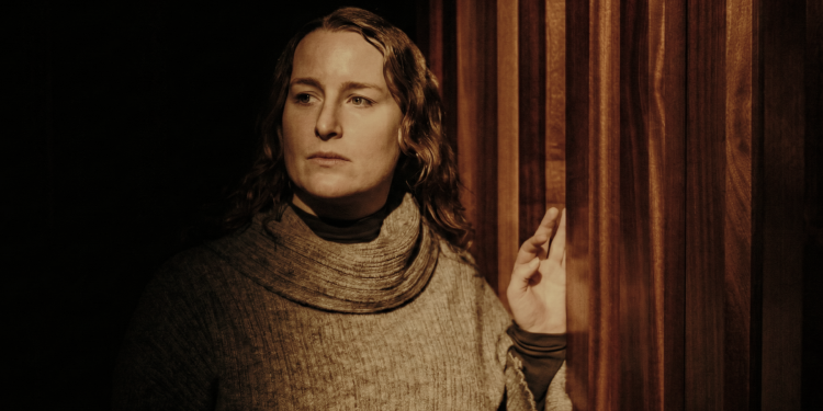 A woman stands by a red partition wall dimly lit