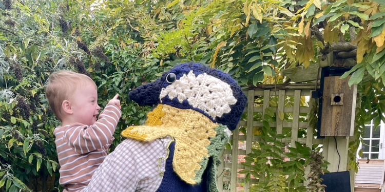A mother wearing a woolen bird headpiece holds a baby