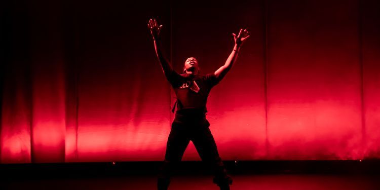 A woman stands in the centre of stage with arms raised