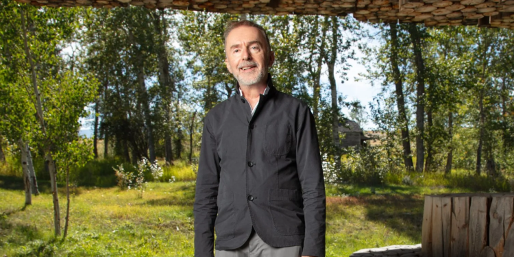 Pedja Muzijevic wearing a dark button up shirt standing in front of a green forest landscape