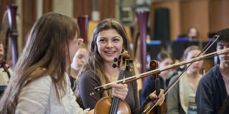 two female musicians smiling at one another holding their instruments
