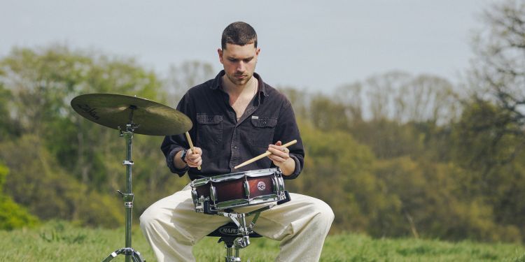 Max Kroon sat on a drum set in the countryside backdrop
