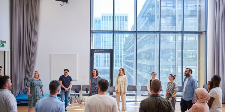 A group of people stood in a circle in a large, bright room