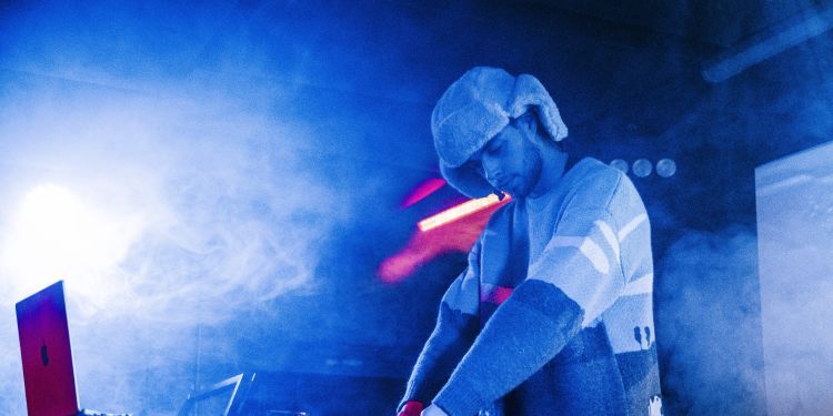 Blue smoke with a DJ playing at decks wearing a long sleeve top and a hat