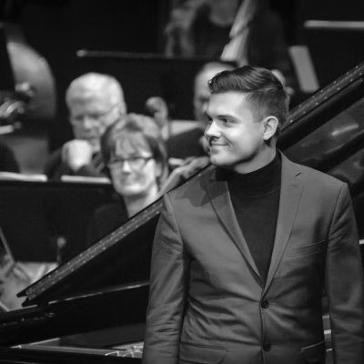Black and white of Jarred Dunn looking away from the camera smiling on stage in front of a piano
