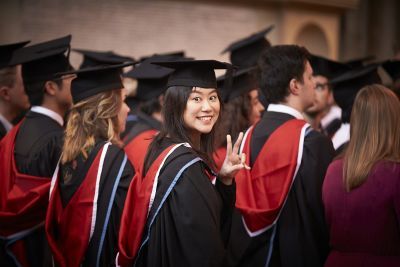 Students in graduation gowns wait in the Great Hall, while one turns and smiles at the camera