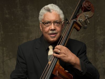 A man in a black suit and tie holds the double bass