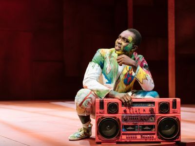 A man wearing a bright coloured suit crouches down by a big red speaker