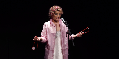 A young woman in a pink lab coat with her hair in curlers holds a broken stethoscope