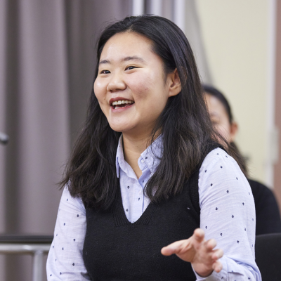 An Asian woman wearing a blue shirt speaks about her research