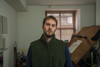 Composer Oliver Leith standing in room looking at the camera with music score on an easel behind him