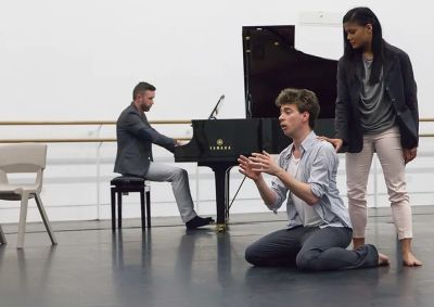 a man sings on the floor, whilst a lady stands behind him, touching his shoulder