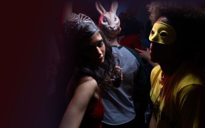 Party scene with person on left wearing a tiara and holding drink, person in middle with rabbit mask on face, person on right with yellow mask over eyes