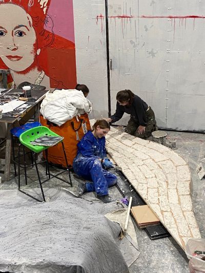 Students in a workshop painting a prop of a bridge