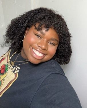 A woman with shoulder length hair leans towards the camera with a big smile