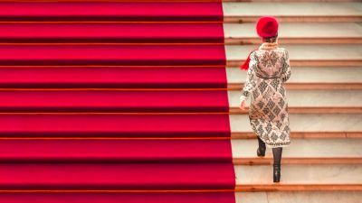 Someone walking up a staircase half in red and half in white. The person walking up the stairs wears a red hat and a white coat