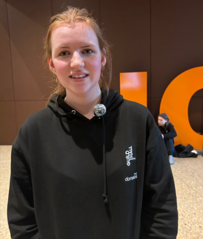 A young musician wearing a black hoodie smiles at the camera at the offices of UCL East