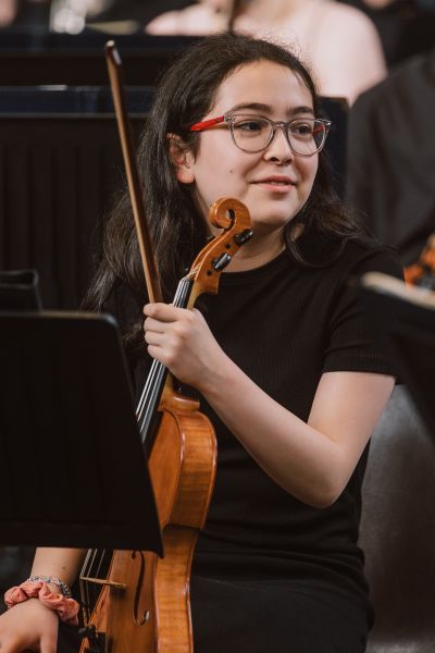Young girl sitting down, holding a violin and looking to the right