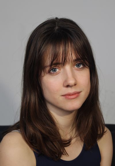 Young white female with brunette hair, taken from the shoulders up, looking directly at camera, slightly smiling