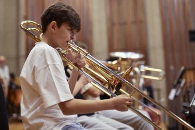 A boy plays a trombone and wears a white t-shirt