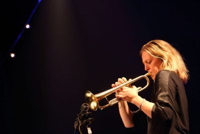 Ingrid Jensen, a white woman with blonde hair plays a trumpet