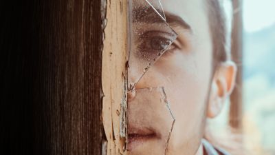 A young man looks through a broken window