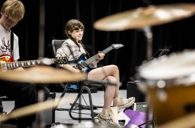 GYA student playing the guitar and smiling while sat down