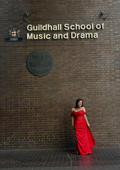 Lily McNeill - BMus Vocal Studies (Soprano) student standing in front on Silk Street 'Guildhall' sign at Graduation