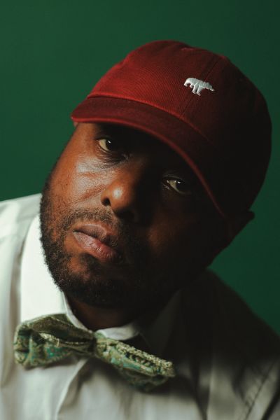 A man with wearing a red cap, white shirt and green bow tie - in head shot image. 